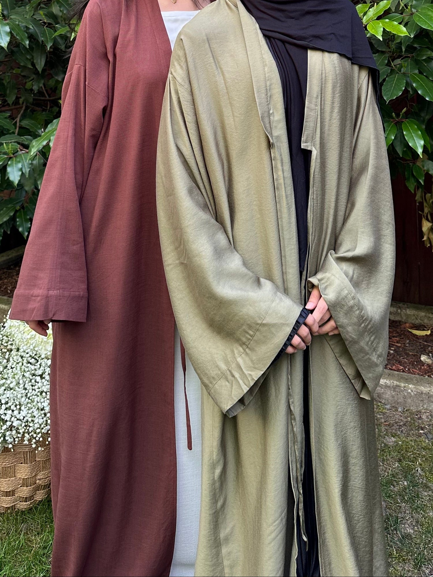 Two women in long dresses standing outdoors with greenery in the background